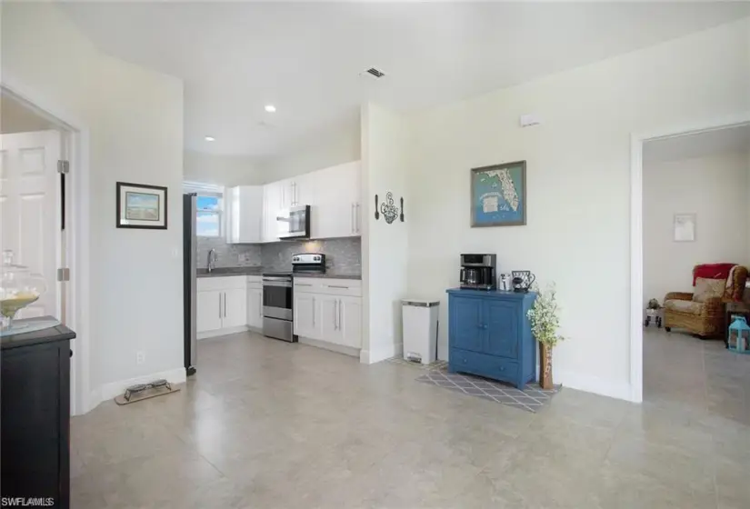 Kitchen featuring backsplash, appliances with stainless steel finishes, white cabinetry, and light tile flooring