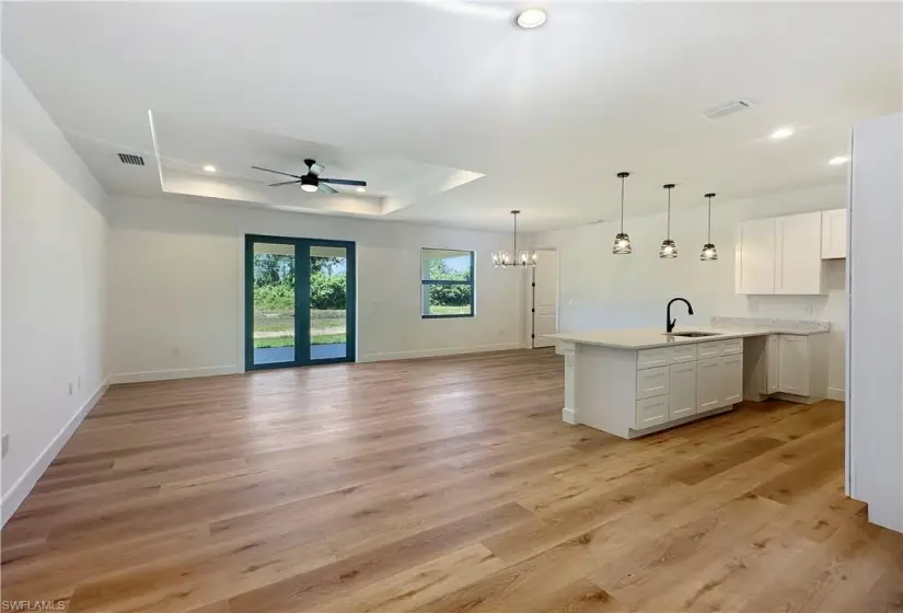 Kitchen featuring a tray ceiling, ceiling fan with notable chandelier, white cabinets, and light wood-type flooring